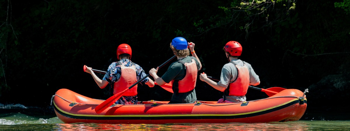 Three travelers paddling inflatable raft on emerald Kolpa River surrounded by forest reflections, eco tourism adventure in pristine nature landscape
