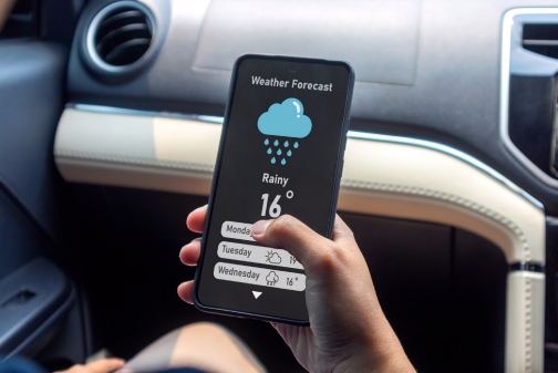moving in the winter: Hand of woman in a car holding a mobile phone to check weather forecast