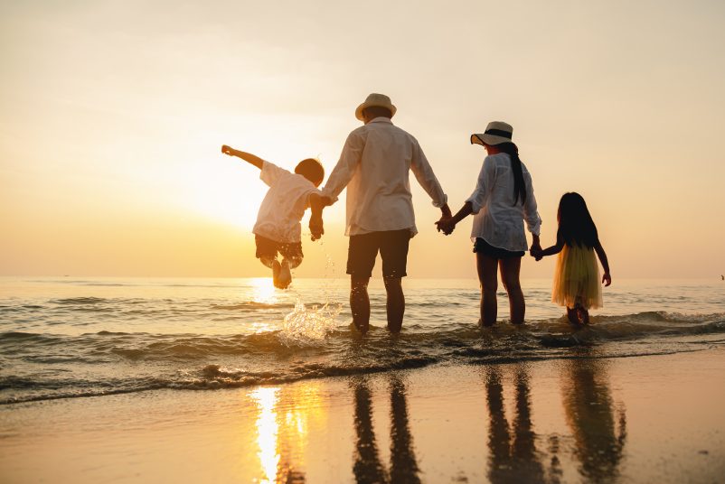 Happy asian family jumping together on the beach in holiday. Silhouette of the family holding hands enjoying the sunset on the beach.Happy family travel and vacations concept.