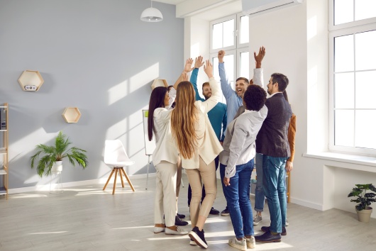 Happy diverse business team celebrating success and having fun all together. Group of cheerful ecstatic people standing in circle in modern office high five each other and shout Yes we did it, Hooray